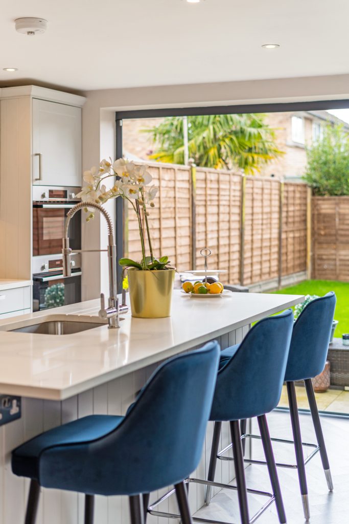 Modern kitchen island with blue velvet bar stools and sliding doors to the garden